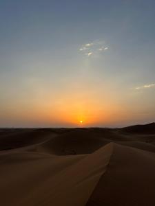 a sunset in the desert with the sun setting in the horizon at Desert tours&trips in Zagora