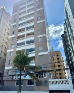 a tall building with a palm tree in front of it at apto frente praia pé na areia 2dorm wifi elevador Smart tv praia grande aviação - leia fotos in Praia Grande