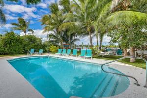 a swimming pool with blue chairs and palm trees at Family Fishing Trip! Jupiter Home with Dock, Hot Tub in Jupiter