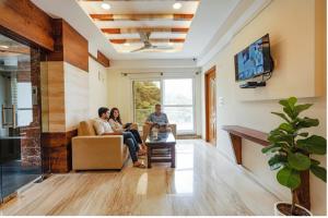three people sitting in a living room watching tv at FabHotel Shakthi Suites - Nr Jayadeva Hospital in Bengaluru