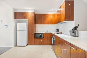 Una cocina con gabinetes de madera y un refrigerador blanco. en Pretty Penthouse - Close to ANU, en Canberra