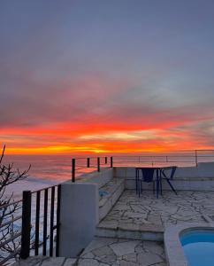 a sunset over the ocean with a table and a bench at Casa Condessa - Create memories in Azenhas do Mar