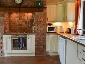 a kitchen with white cabinets and a brick wall at Mill Cottage in Mathon