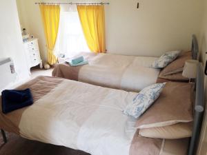 two beds in a bedroom with yellow curtains at Jug And Glass Cottage in Upper Langwith
