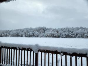 a fence covered in snow with a field and trees at Chalet L'Apéro des Chutes - Spa, détente & nature au bord de l'eau en Mauricie in  Notre-Dame de Montauban