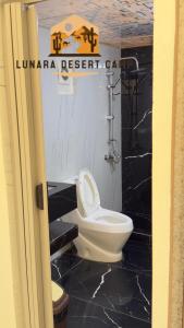 a bathroom with a white toilet and a black floor at Lunara Desert Camp in Wadi Rum