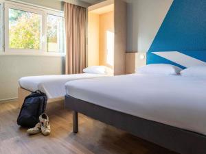 een hotelkamer met twee bedden en een rugzak op de vloer bij ibis budget Tours Sud in Chambray-lès-Tours