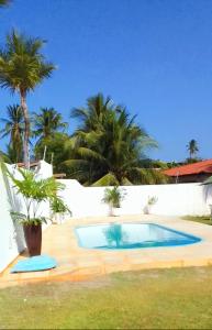 a swimming pool in front of a white wall with palm trees at Wind Villa Cumbuco - Casa in Cumbuco
