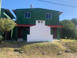 a green and white house with a white building at Puerto del sol in Punta Del Diablo