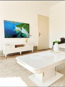 een witte woonkamer met een grote tv aan de muur bij Gold Apartments in Novi Pazar