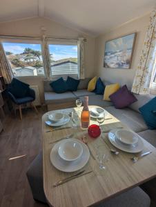 a table with plates and wine glasses on it in a living room at Modern Style Pet Friendly Holiday Home sited on Durdle Door Holiday Park in West Lulworth +10 photos