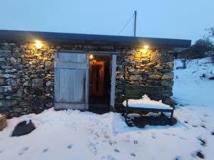 Mountain Cottage with Barn Sauna, Clonbur, Galway في Clonbur: مبنى حجري مع باب في الثلج