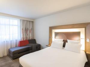 a hotel room with a white bed and a chair at Novotel Lyon Bron Meeting & Events in Bron