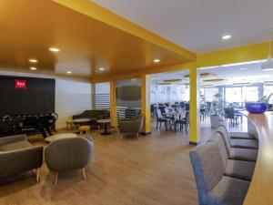 a waiting room with chairs and tables and a screen at ibis Montélimar Nord in Saulce-sur-Rhône
