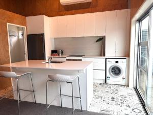 a kitchen with white cabinets and a counter with stools at The Black Shed Studio in New Plymouth +2 photos