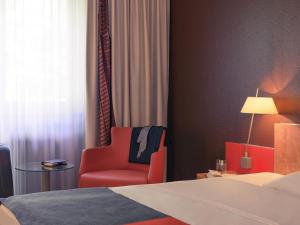 a hotel room with a bed and a red chair at Mercure Residenz Frankfurt Messe in Frankfurt/Main