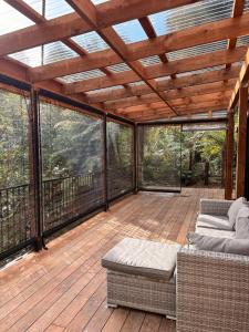 a screened in porch with a couch and tables on a deck at Mamaku Hideaway - with outdoor bath in Greymouth +10 photos
