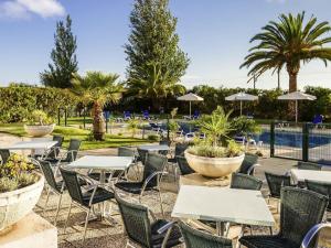a group of tables and chairs with trees and a pool at Hotel ibis Faro Algarve in Faro