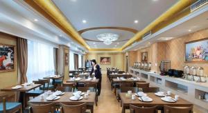 a woman standing in a restaurant with tables and chairs at Vienna Hotel Anhui Xuancheng High-Speed Railway Station in Xuancheng