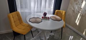 ein weißer Tisch mit zwei gelben Stühlen und einem Teller mit Essen in der Unterkunft Studio Premium in Târgu Jiu