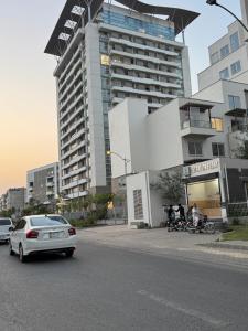 a white car driving down a street with a tall building at Penta Square Modern & Luxury Apartments City View DHA Lahore in Lahore