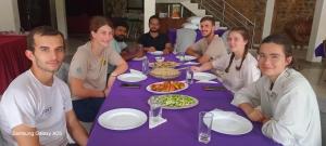 a group of people sitting around a purple table with food at Sinharaja Cottage in Nelluwa