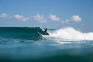 una persona montando una ola en una tabla de surf en el océano en Long Beach Laamu Hotel, en Gan