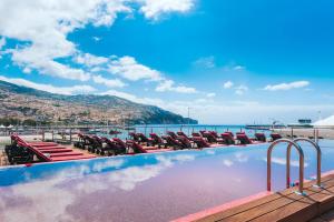 uma piscina com espreguiçadeiras e o oceano em Pestana CR7 Funchal em Funchal