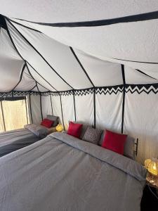 a bed in a tent with red pillows on it at Bivouac Erg Chegaga Nomademoi in El Gouera