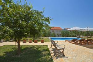 a pool with a bench and a tree and chairs at D&N Apartment in Kaštela