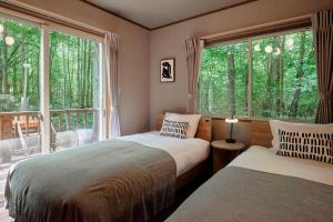 a bedroom with two beds and a large window at Villa Noël Kitakaruizawa Jardin Forest Sauna Hideaway in Tsumagoi