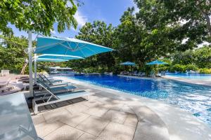 a swimming pool with lounge chairs and a blue umbrella at Jungle Studio at Tambuli Ocean View by Dominik Studio with Pool & Balcony in Mactan in Lapu Lapu City