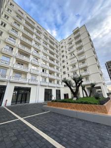 a large white building with a tree in a parking lot at Apartment in Kamëz