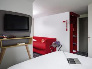 Una habitación con una silla roja y un televisor. en ibis Styles Chartres Métropole, en Chartres