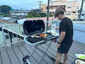 a man standing next to a grill on a balcony at 一棟貸しハウスまれち in Kumejima