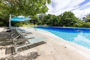 a row of lounge chairs with an umbrella next to a swimming pool at Dominiks quite and Elegant Studio Ocean View Pool at Tambuli Resort High Floor in Maribago