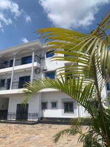 a white building with a palm tree in front of it at Aloha Suites Odza - by Skyline Residence Services in Yaoundé