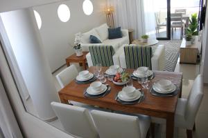 ein Wohnzimmer mit einem Holztisch und weißen Stühlen in der Unterkunft Luxurious 3-bedroom Bloubergstrand Cape Town beachfront apartment with stunning sea and beach view in Cape Town