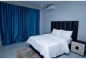 a bedroom with a large white bed and blue curtains at Akwaaba Apartments in Chipata