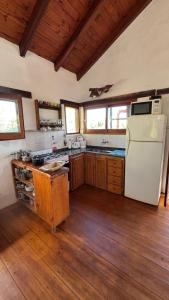 a kitchen with a white refrigerator and wooden floors at Cabaña de montaña con pileta en hermoso predio in Villa Yacanto