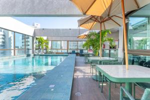 a pool with tables and umbrellas in a building at Boa Viagem - FLAT ROOFTOP 470 - NOVO in Recife