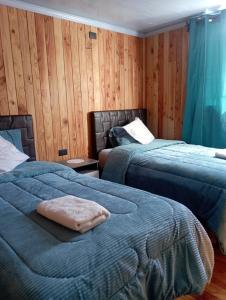 two beds in a room with wooden walls at Casamaiga hostal in Chaitén
