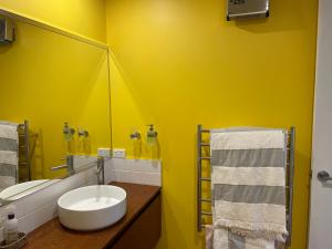 Baño amarillo con lavabo y espejo en Oakhampton Lodge, en Kaiapoi