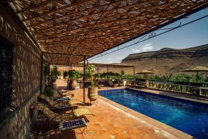 a swimming pool with chairs and a patio with mountains in the background at La Terrasse des Delices in Ouarzazate