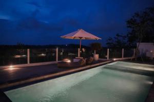 a swimming pool at night with an umbrella at Cavahills Cottage in Denpasar