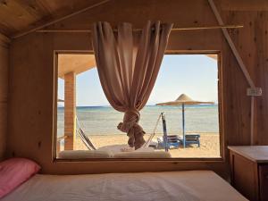a bedroom with a window with a hammock and a beach at Leley Camp in Nuweiba