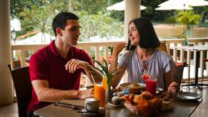 Ein Mann und eine Frau sitzen an einem Tisch und telefonieren mit einem Handy. in der Unterkunft FCC Angkor by Avani in Siem Reap
