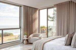a bedroom with a bed and a chair and large windows at Salt & Sand in Wilderness +80 photos