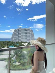 a woman in a white dress and a hat on a balcony at The Light Arena Ocean Tower in Cam Ranh International Airport