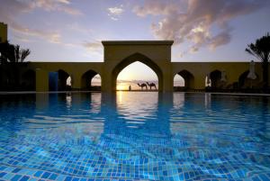 a swimming pool with a sunset in the background at Tilal Liwa Desert Retreat in Madīnat Zāyid